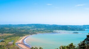Pemandangan udara Geopark Ciletuh yang luas, menampilkan teluk berbentuk tapal kuda, pantai berpasir, dan perbukitan hijau yang rimbun.