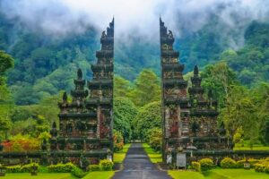 Gerbang candi tradisional Bali dengan latar belakang pegunungan hijau berkabut.